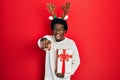 Young african american man wearing deer christmas hat holding gift pointing displeased and frustrated to the camera, angry and Royalty Free Stock Photo