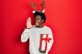 Young african american man wearing deer christmas hat holding gift shouting and screaming loud to side with hand on mouth Royalty Free Stock Photo