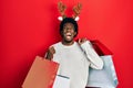 Young african american man wearing deer christmas hat holding shopping bags angry and mad screaming frustrated and furious, Royalty Free Stock Photo