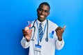 Young african american man wearing doctor uniform holding heart pointing thumb up to the side smiling happy with open mouth Royalty Free Stock Photo