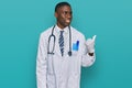 Young african american man wearing doctor uniform and stethoscope smiling with happy face looking and pointing to the side with Royalty Free Stock Photo