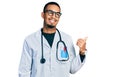 Young african american man wearing doctor uniform and stethoscope smiling with happy face looking and pointing to the side with Royalty Free Stock Photo