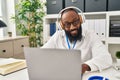 Young african american man wearing doctor uniform using laptop and headphones working at clinic Royalty Free Stock Photo