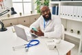 Young african american man wearing doctor uniform using smartphone working at clinic Royalty Free Stock Photo