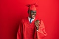 Young african american man wearing graduation cap and ceremony robe angry and mad raising fist frustrated and furious while Royalty Free Stock Photo