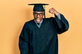 Young african american man wearing graduation cap and ceremony robe angry and mad raising fist frustrated and furious while Royalty Free Stock Photo