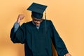 Young african american man wearing graduation cap and ceremony robe dancing happy and cheerful, smiling moving casual and Royalty Free Stock Photo