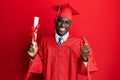 Young african american man wearing graduation cap and ceremony robe holding diploma screaming proud, celebrating victory and Royalty Free Stock Photo