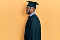 Young african american man wearing graduation cap and ceremony robe looking to side, relax profile pose with natural face and Royalty Free Stock Photo