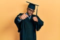 Young african american man wearing graduation cap and ceremony robe punching fist to fight, aggressive and angry attack, threat Royalty Free Stock Photo