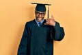 Young african american man wearing graduation cap and ceremony robe smiling doing phone gesture with hand and fingers like talking Royalty Free Stock Photo