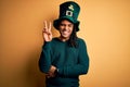 Young african american man wearing green hat with clover celebrating saint patricks day smiling with happy face winking at the