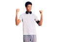 Young african american man wearing gym clothes and using headphones screaming proud, celebrating victory and success very excited Royalty Free Stock Photo