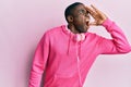 Young african american man wearing gym clothes and using headphones shouting and screaming loud to side with hand on mouth Royalty Free Stock Photo