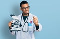 Young african american man wearing scientist uniform holding microscope annoyed and frustrated shouting with anger, yelling crazy
