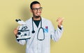 Young african american man wearing scientist uniform holding microscope pointing thumb up to the side smiling happy with open Royalty Free Stock Photo