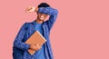 Young african american man wearing student backpack holding book smiling cheerful playing peek a boo with hands showing face