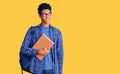 Young african american man wearing student backpack holding book smiling looking to the side and staring away thinking Royalty Free Stock Photo