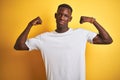 Young african american man wearing white t-shirt standing over isolated yellow background showing arms muscles smiling proud Royalty Free Stock Photo