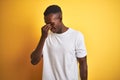 Young african american man wearing white t-shirt standing over  yellow background tired rubbing nose and eyes feeling Royalty Free Stock Photo