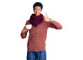 Young african american man wearing winter scarf and drinking a cup of hot coffee smiling happy and positive, thumb up doing Royalty Free Stock Photo