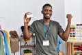 Young african american man working as manager at retail boutique holding credit card pointing thumb up to the side smiling happy Royalty Free Stock Photo