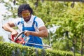 Young african american man in working suit using electric trimmer to cut hedge outdoor, gardening Royalty Free Stock Photo