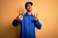 Young african american mechanic man wearing blue uniform and cap over yellow background smiling looking to the camera showing Royalty Free Stock Photo