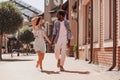 Young african american man and woman holding hands and walking on the street at daytime, full length shot