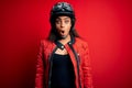 Young african american motorcyclist girl wearing moto helmet and glasses over red background afraid and shocked with surprise Royalty Free Stock Photo