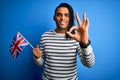 Young african american patriotic man with dreadlocks holding united kingdom flag doing ok sign with fingers, excellent symbol Royalty Free Stock Photo