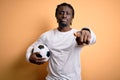 Young african american player man playing soccer holding football ball over yellow background pointing with finger to the camera Royalty Free Stock Photo