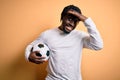 Young african american player man playing soccer holding football ball over yellow background stressed with hand on head, shocked Royalty Free Stock Photo