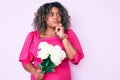 Young african american plus size woman holding flowers serious face thinking about question with hand on chin, thoughtful about