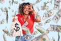 Young african american plus size woman holding money bag with dollar symbol smiling happy doing ok sign with hand on eye looking Royalty Free Stock Photo