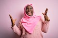 Young african american plus size woman wearing muslim hijab over isolated pink background crazy and mad shouting and yelling with Royalty Free Stock Photo