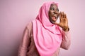 Young african american plus size woman wearing muslim hijab over isolated pink background shouting and screaming loud to side with Royalty Free Stock Photo