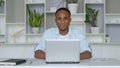 Young African-American is sitting at Home Office, smiling at the Camera. Portrait of Satisfied Young Man is working on Royalty Free Stock Photo