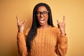 Young african american smart woman wearing glasses and casual sweater over yellow background shouting with crazy expression doing Royalty Free Stock Photo