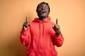 Young african american sporty man wearing sweatshirt with hoodie over yellow background amazed and surprised looking up and Royalty Free Stock Photo