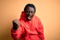 Young african american sporty man wearing sweatshirt with hoodie over yellow background angry and mad raising fist frustrated and Royalty Free Stock Photo