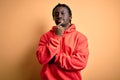 Young african american sporty man wearing sweatshirt with hoodie over yellow background looking confident at the camera with smile Royalty Free Stock Photo