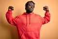 Young african american sporty man wearing sweatshirt with hoodie over yellow background showing arms muscles smiling proud Royalty Free Stock Photo