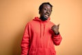 Young african american sporty man wearing sweatshirt with hoodie over yellow background smiling with happy face looking and Royalty Free Stock Photo