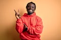 Young african american sporty man wearing sweatshirt with hoodie over yellow background smiling with happy face winking at the Royalty Free Stock Photo