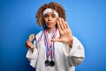 Young african american sporty woman with curly hair doing sport winning medals with open hand doing stop sign with serious and