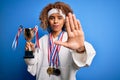 Young african american sporty woman doing sport winning medals and trophy with open hand doing stop sign with serious and