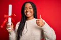 Young african american student girl holding university diploma over red isolated background happy with big smile doing ok sign, Royalty Free Stock Photo