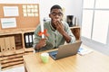 Young african american student man holding graduate degree diploma sitting on the table covering mouth with hand, shocked and Royalty Free Stock Photo