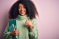 Young african american student woman with afro hair reading books over pink background happy with big smile doing ok sign, thumb Royalty Free Stock Photo